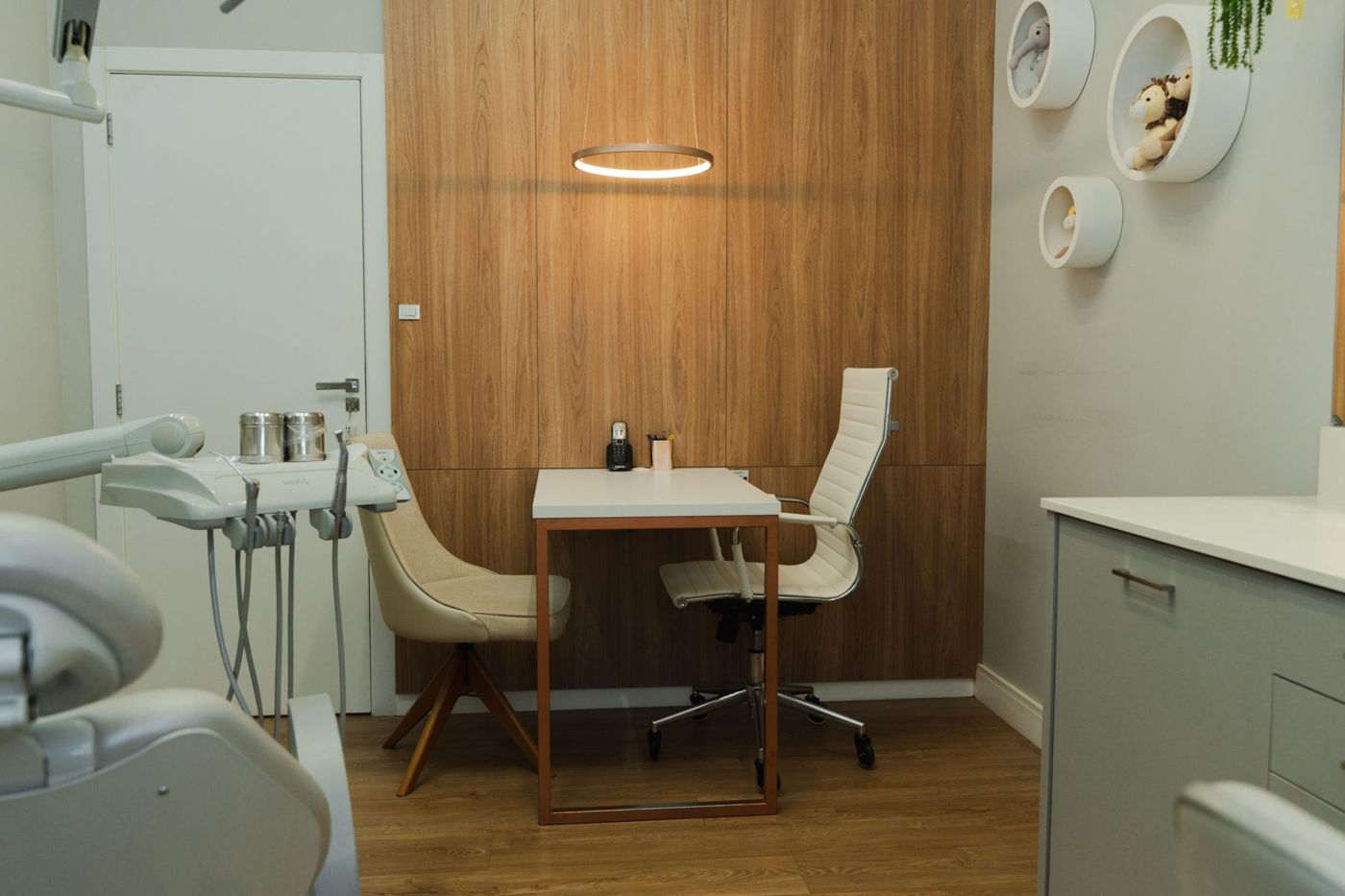 Consultório da OrtoHaus com mesa de conversa, pendente de luz cobre e parede de madeira