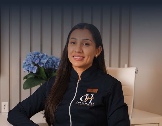 Dra. Ana Cláudia da Silva no consultório, uniforme navy com o monograma OH